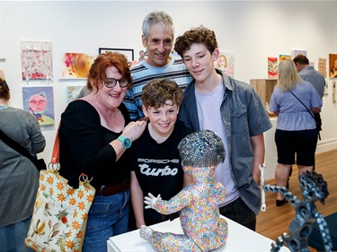 A family smiling and looking at a sequinned Artz Blitz statue in the gallery.