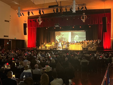 Bobby Fox and the Mordialloc Jazz Orchestra on stage at Kingston City Hall, in front of a crowd seated at tables.