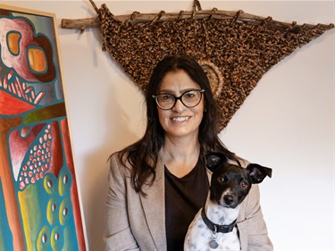 Artist Adriana Di Stasio smiling in front of artwork and holding her dog