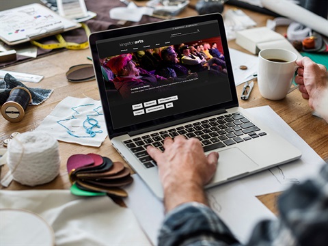 The new Arts website shown on a laptop with a persons hand on the keyboard