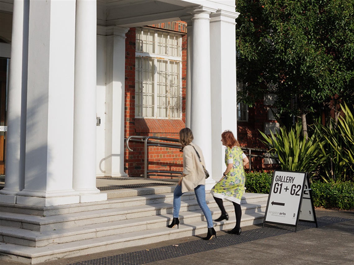 Two people walking up steps to enter building with while columns