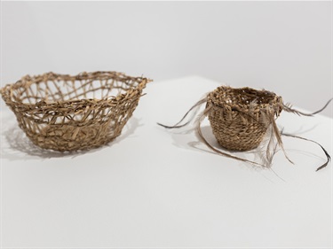 Two small, handwoven baskets, made with river reeds and emu feathers, against a white background