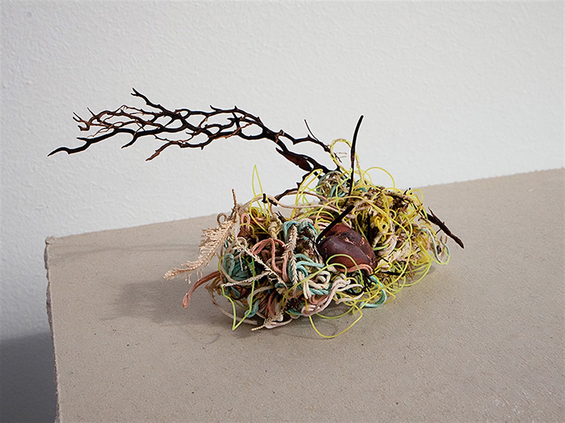 A photo of a small sculpture made of found objects such as colourful string, and dried seaweed