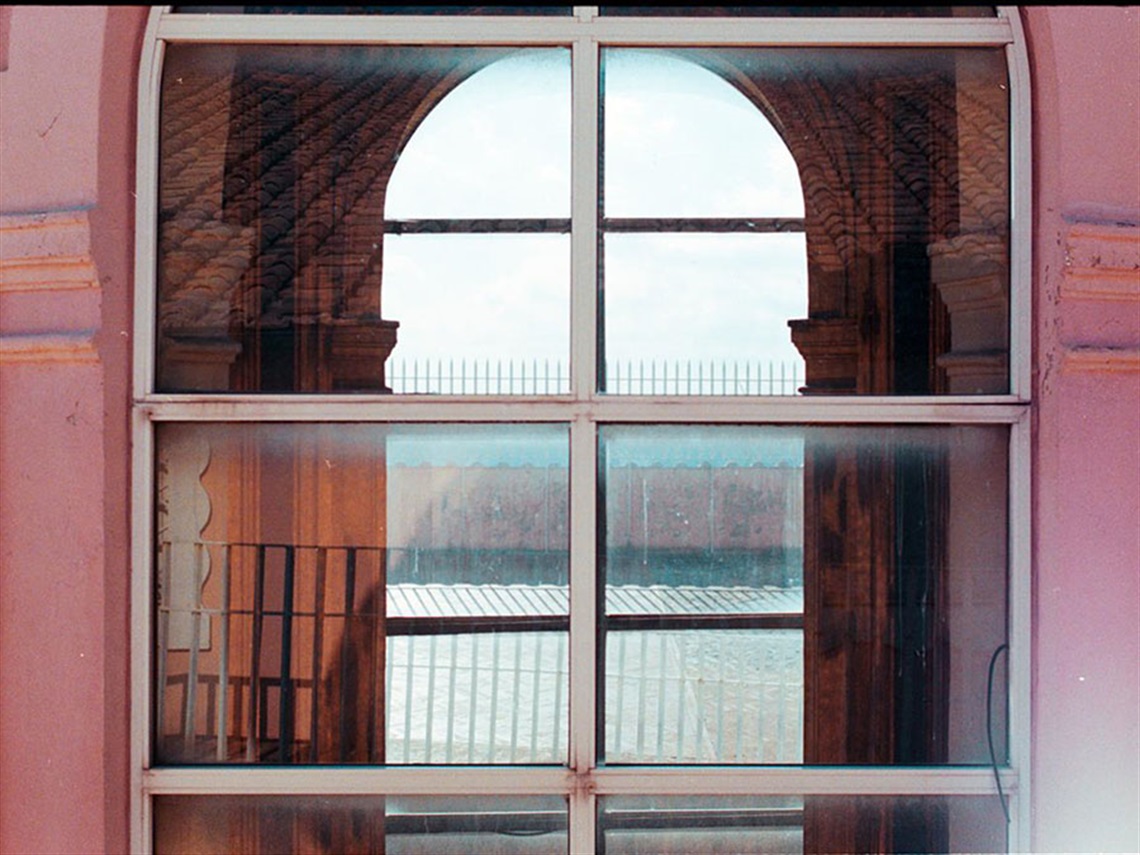 a colourful photo of a close-up of a building window, with the reflection of other infrastructure in the glass