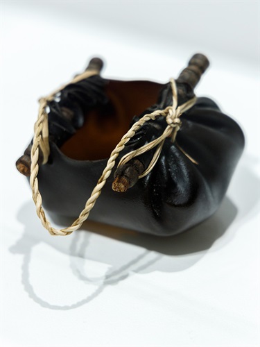 A water carrier, made of Brown-yellow Bull Kelp, She-oak sticks, river reed. Resembling a small leather bag with open top, against a white background.