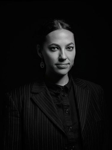 Black and white head and shoulders portrait image of a female with drop earrings, dark blazer and dark collared top