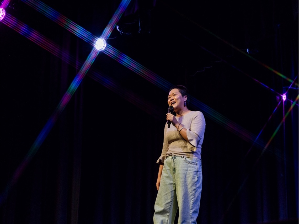 A person holding a microphone on a stage with blue lights behind them.