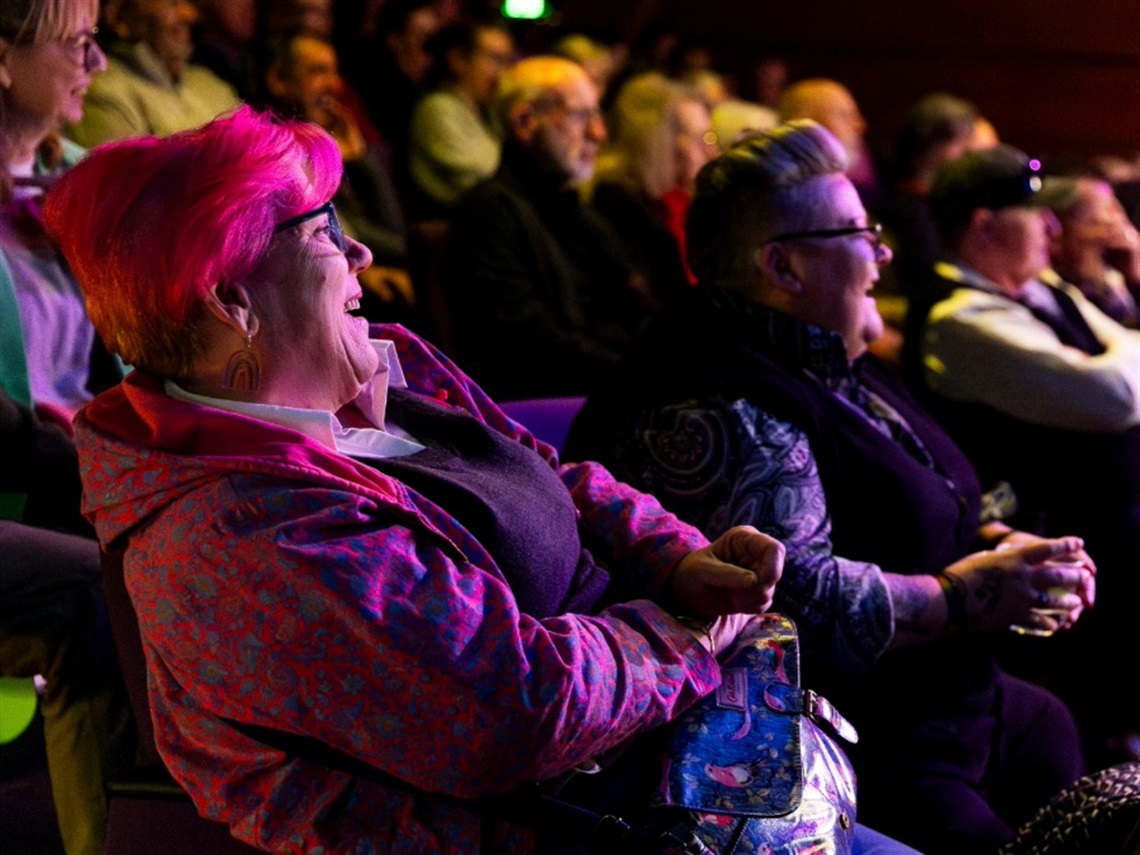 An audience in a theatre seated facing a stage and laughing