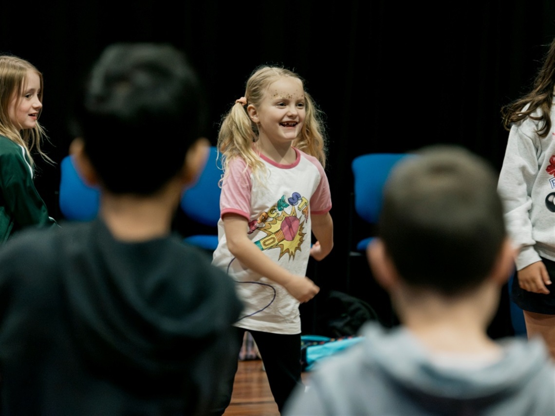 A girl smiling and dancing surrounded by a circle or other children