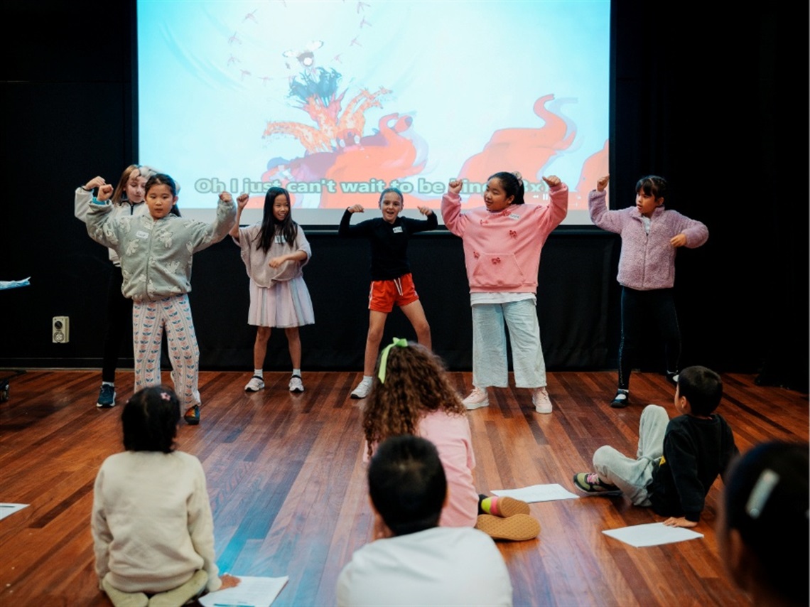 A group of children perform a song and dance in front of other children.