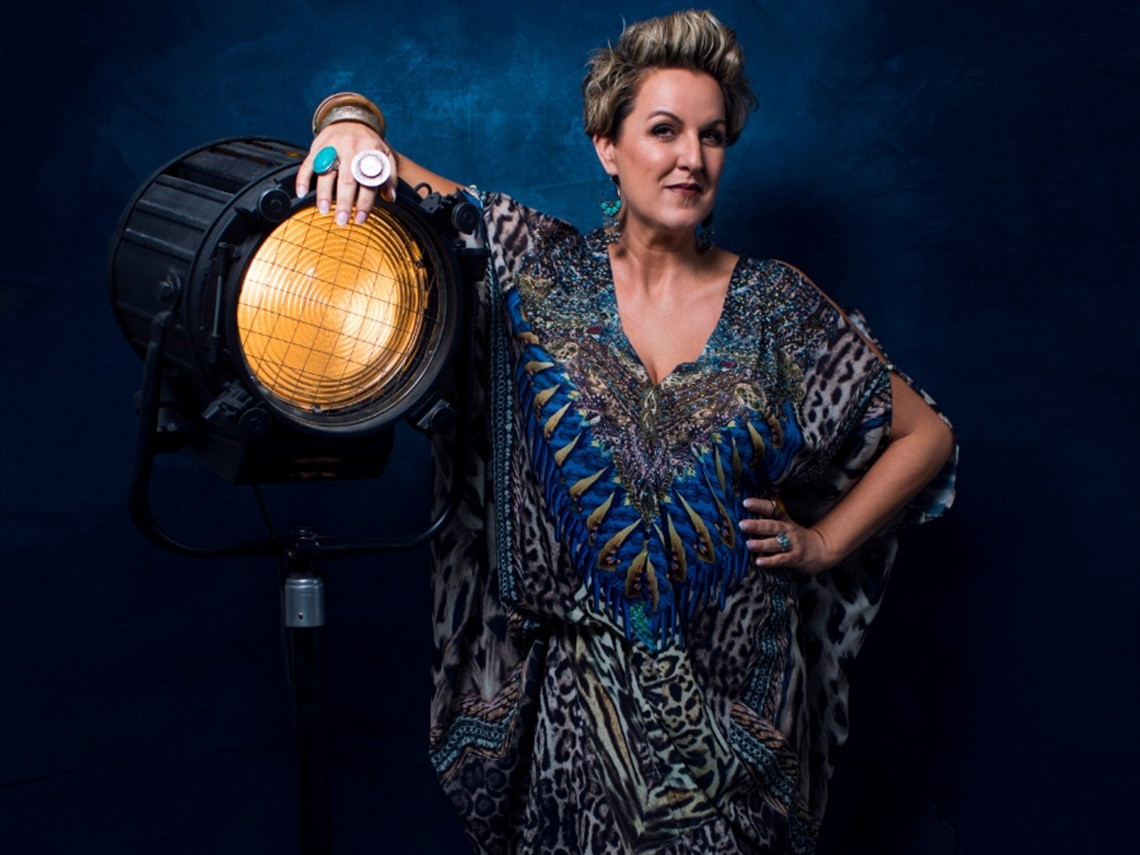 A woman in a blue kaftan leans against a large light
