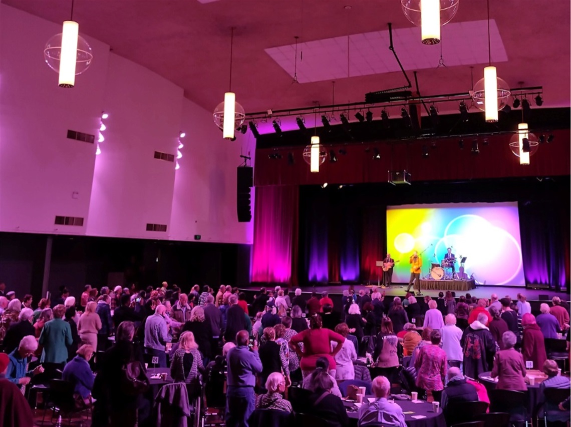A large audience watches and dances to a band on a stage