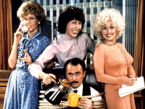 Three women surround a man who is tied up with rope and being poured a coffee. All women are smiling at the camera