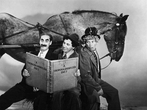 Three men sit in front of a large horse reading a big book