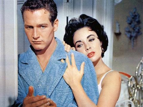 A man wears a blue robe while a woman stands behind him with her hand on his shoulder