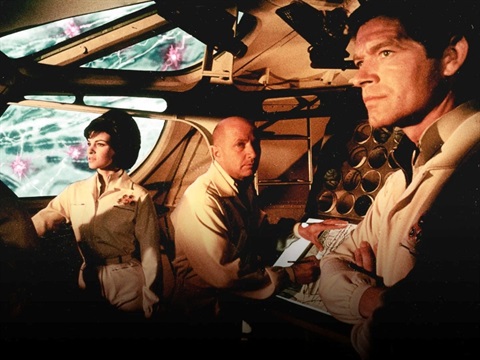 Three people standing in a spaceship looking concerned and staring out the front window