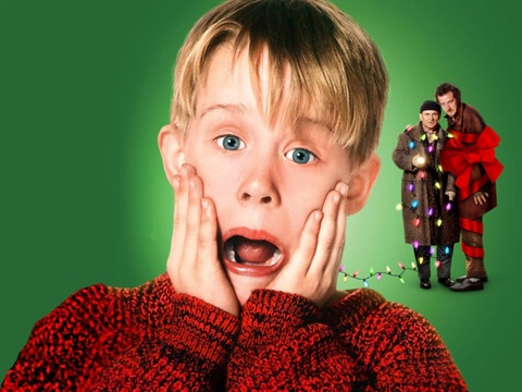 A young boy has a shocked expression whilst two men covered in ribbon and Christmas lights are in the background
