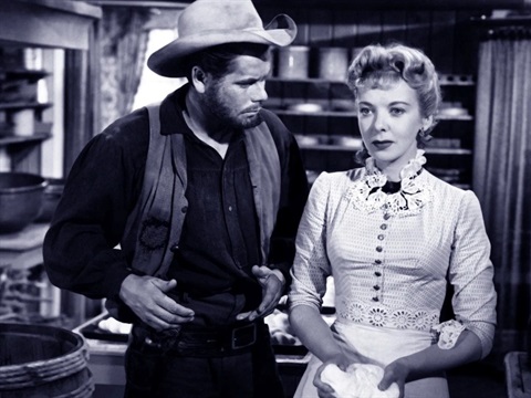 A man wearing a cowboy hat stares down at a lady. The image is black and white