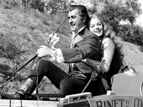 A man and a woman on a horse and carriage with the woman holding onto the man and smiling