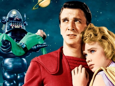 A robot holds a person wearing a green jumpsuit and a man and woman stare out to their right. The background is space with a planet in the image.