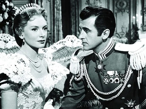 A man and woman sitting next to each other wearing Royal clothing. The man is gazing at the woman.