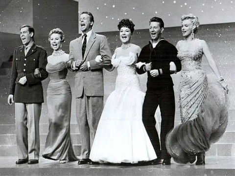 Six people stand in a horizontal line wearing formalwear on a stage