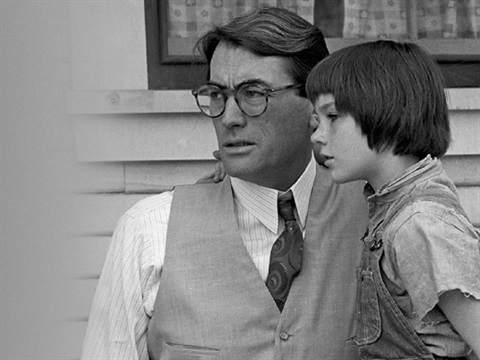 A father has his daughter on his lap and they are both looking out into the distance. The father wears glasses and the daughter is very young