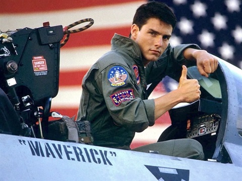 Man sitting in a fighter jet wearing a cargo green jumpsuit with thumb up