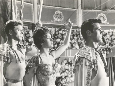 Two men and a woman facing an audience with their hands up after a trapeze performance 