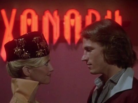 A man and woman stare at each other with Xanadu in big red neon lights behind them