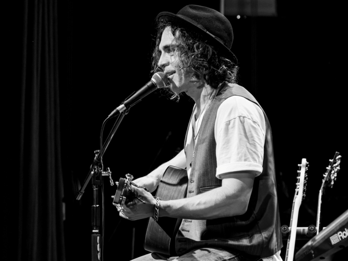 Close up of a musician playing the guitar and singing into a microphone while sitting down.