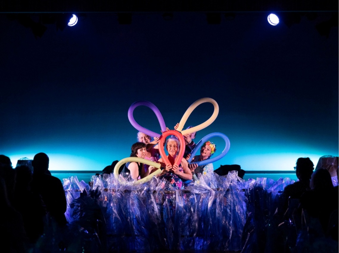 Women stand on a stage with pool noodles surrounding their faces.