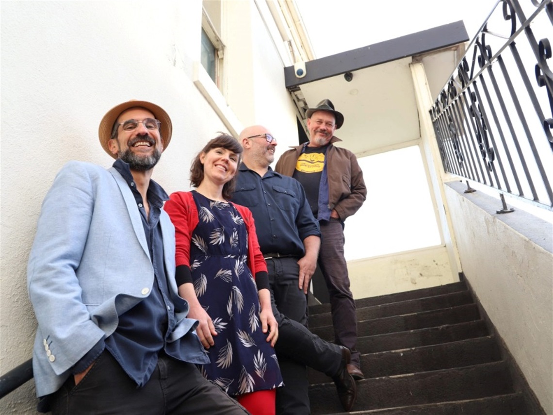 Four people stand on a staircase looking down at the camera.