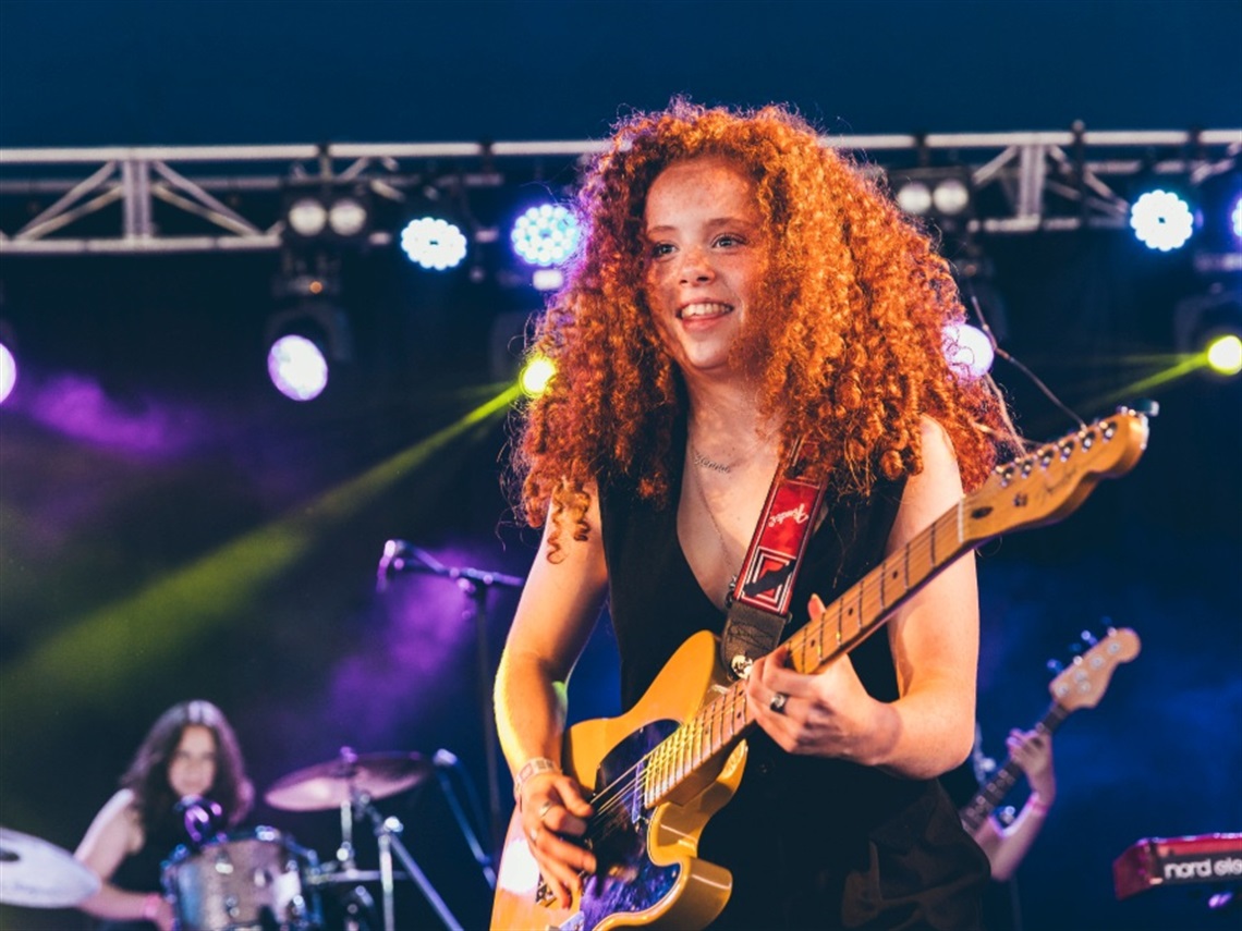 Girl standing on stage holding a yellow guitar.