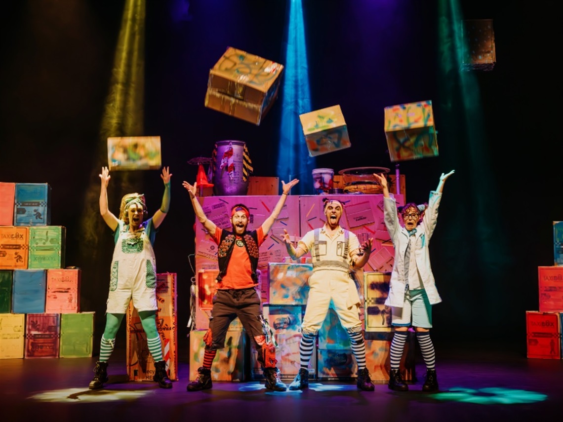 Four performers on stage throwing cardboard boxes in the air