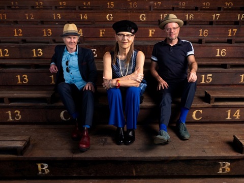 Two men and a woman sit on wooden steps with the woman sitting in the middle.