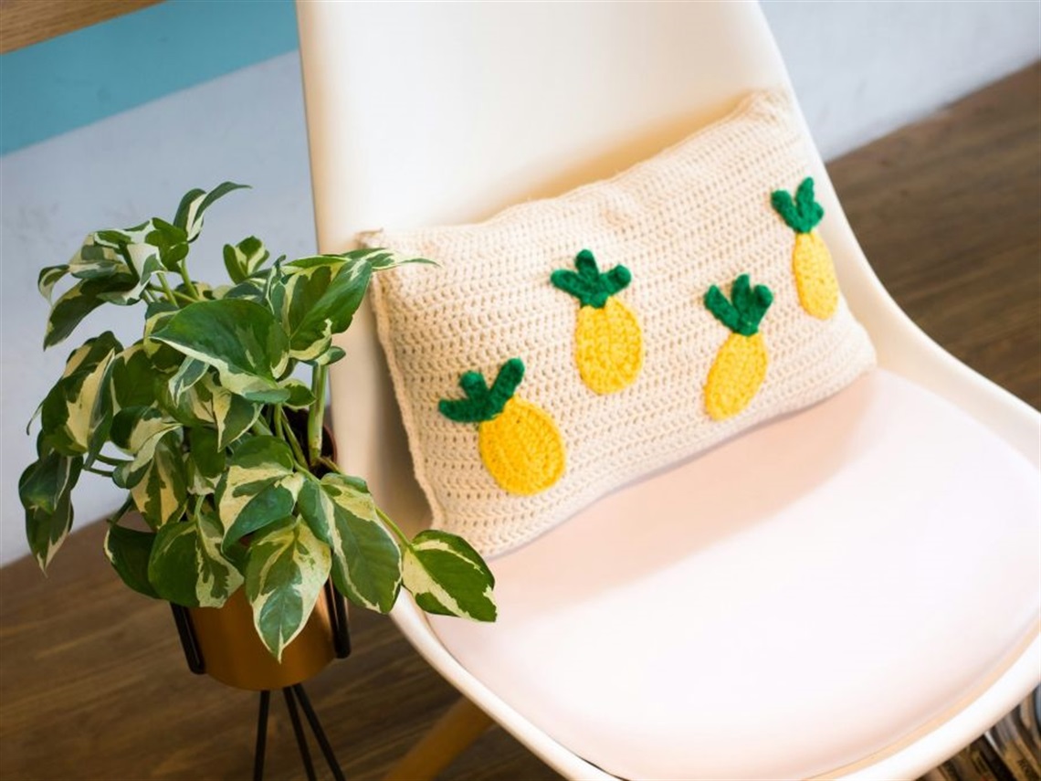 House plant, white chair with a crochet white cushion with pineapples on it.