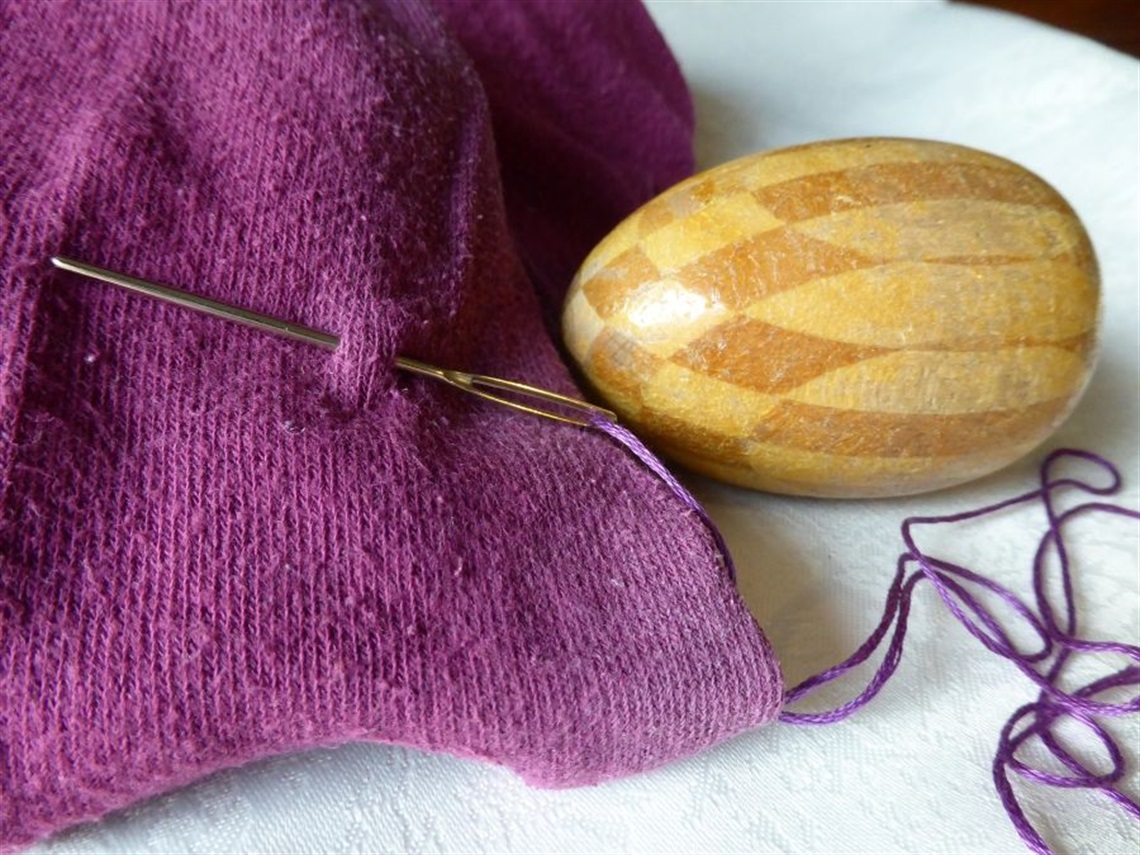 section of purple knit with darning needle and wooden egg