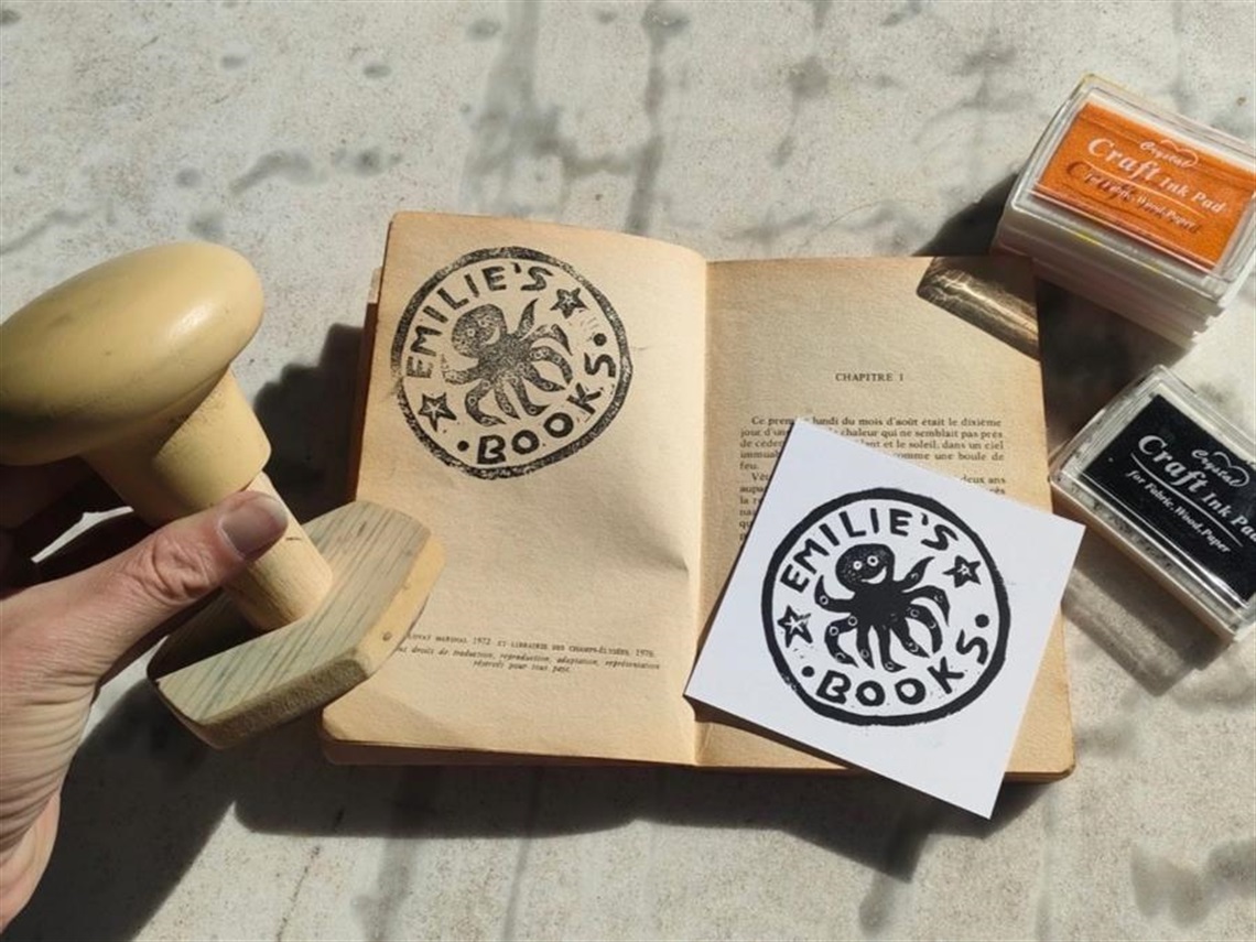A hand holding a wooden bookplate stamp over an open book