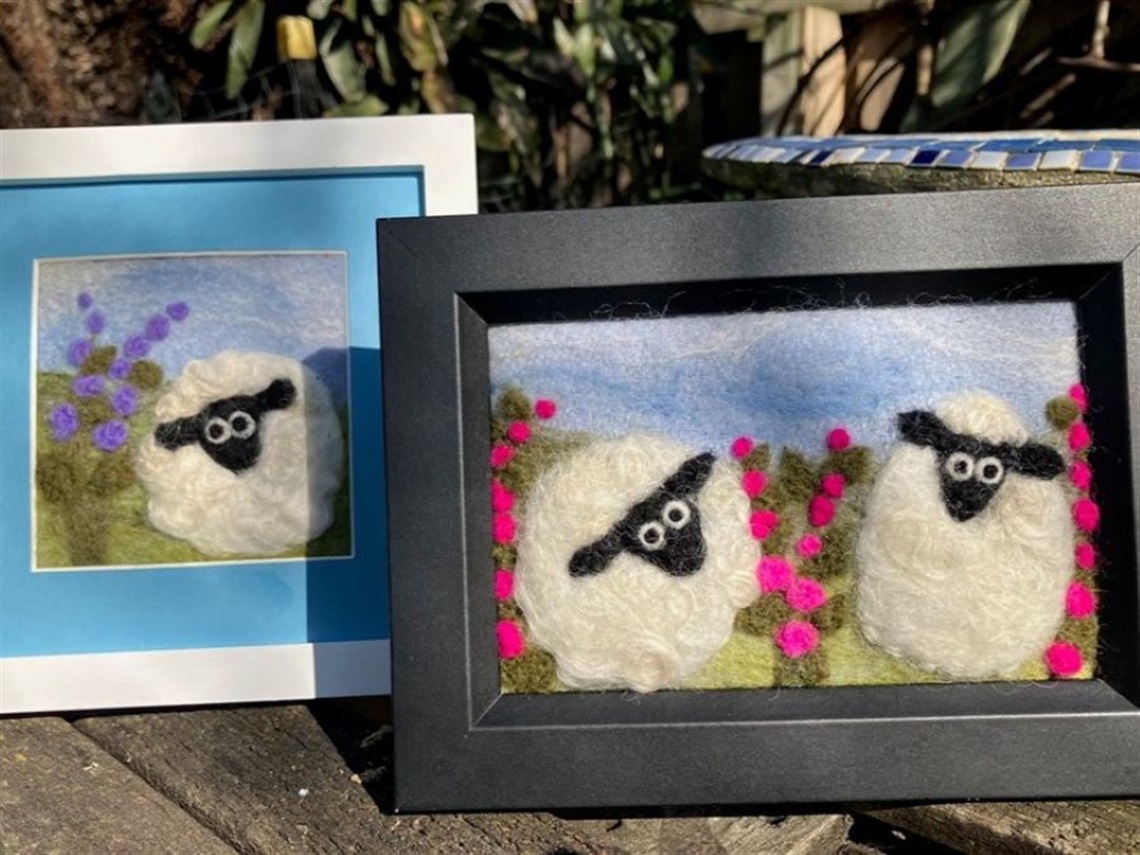 2 frames containing 2 felted artworks featuring sheep in a field. 