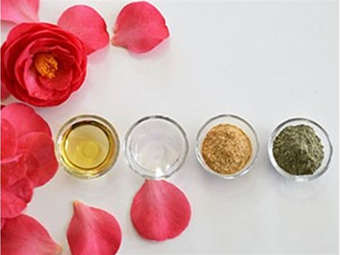Four small bowls containing oil and powders surrounded by red petals
