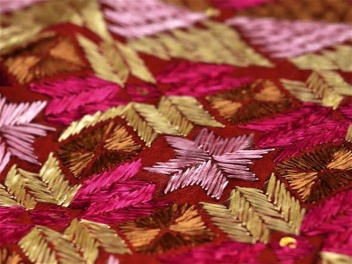 Indian embroidery of geometric motifs in bright pinks and golds on red fabric