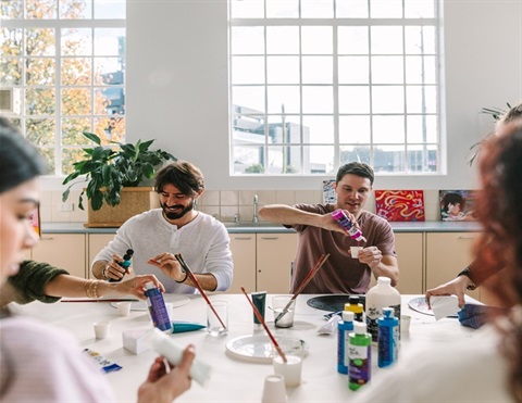 People sitting around a table smiling and participating in an art workshop