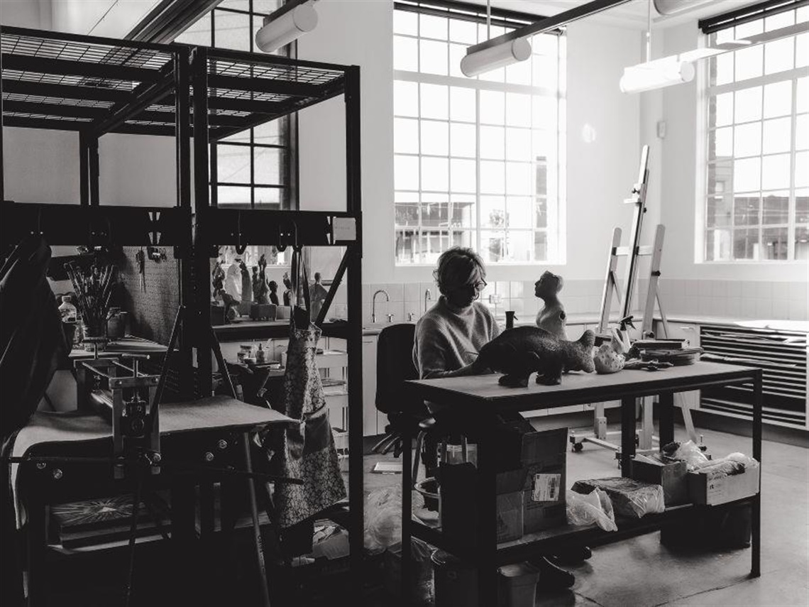 Black and white image of seated female with ceramic artwork in artist studio