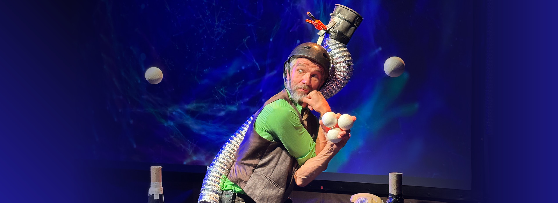 Jens Altheimer wearing a green shirt and bike helment, juggling five balls.