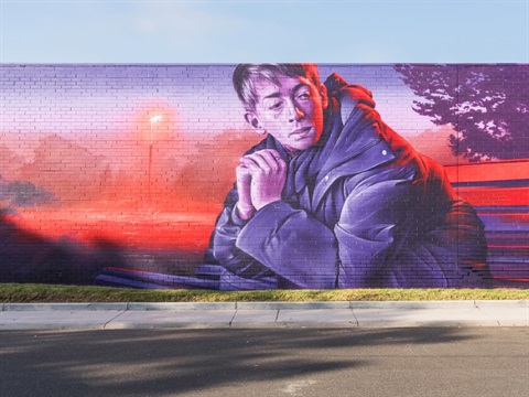 Large-scale mural by artist Smug, painted at Wall to Wall Mordi Village 2024, depicting a man seated on a park bench.
