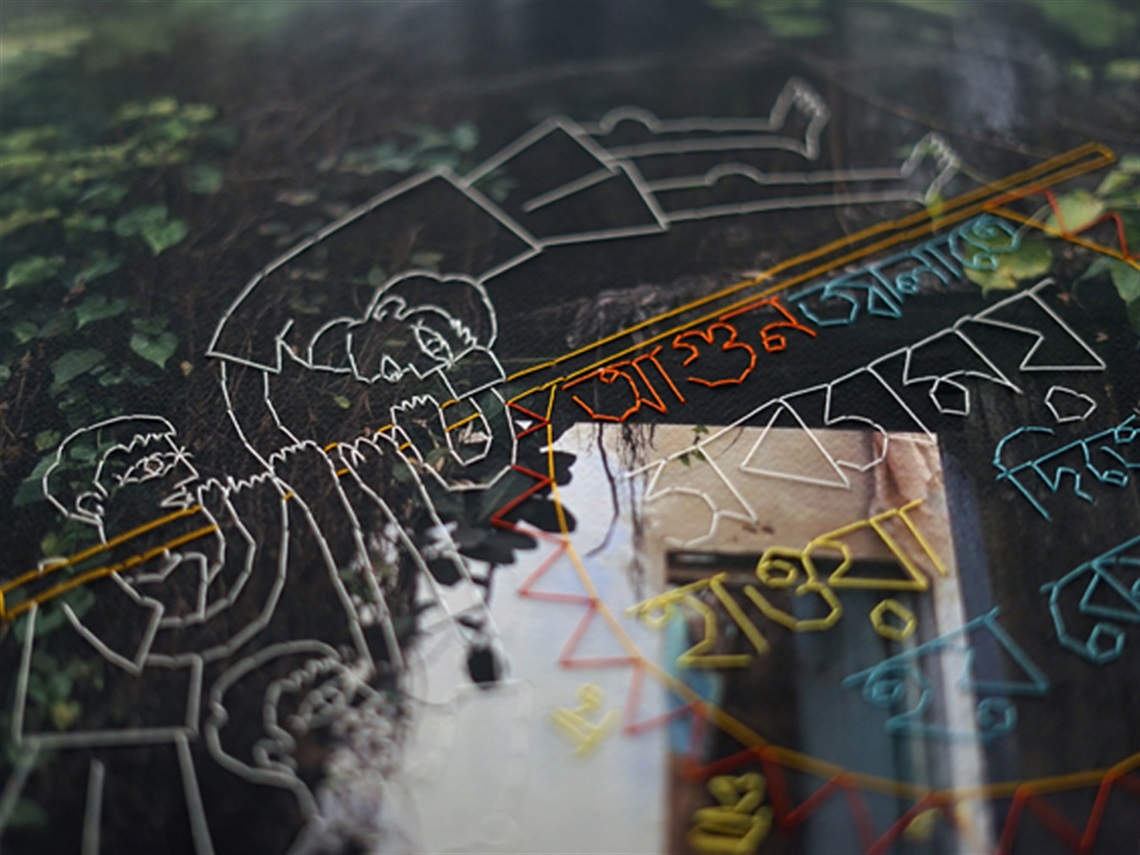 A close-up photo of colourful stitching of two people and text on a photo of green foliage