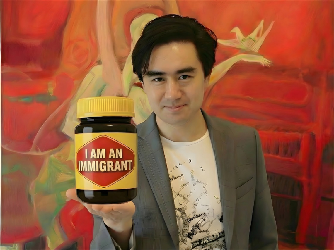 An Asian man holding a jar of vegemite with the label I am an immigrant